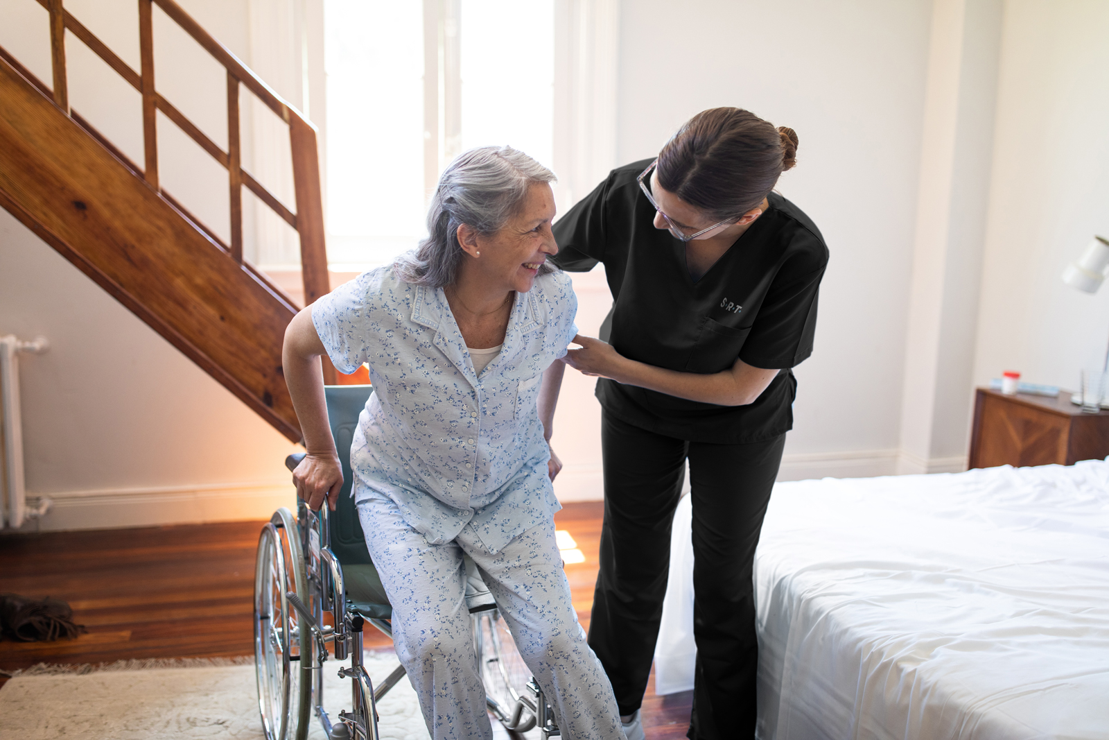 A caregiver helps an elderly woman into a wheelchair
