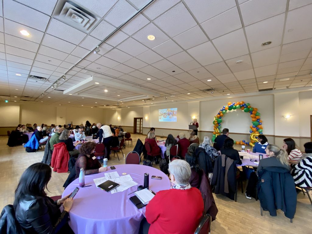 A large room filled with people listening to someone speaking on a stage.
