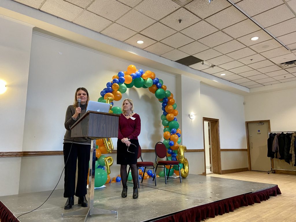 A person speaking at a podium while another person looks on.