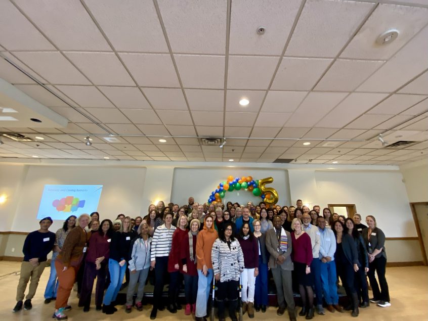 A group of people standing in a room and smiling. A balloon arch is visible behind them.