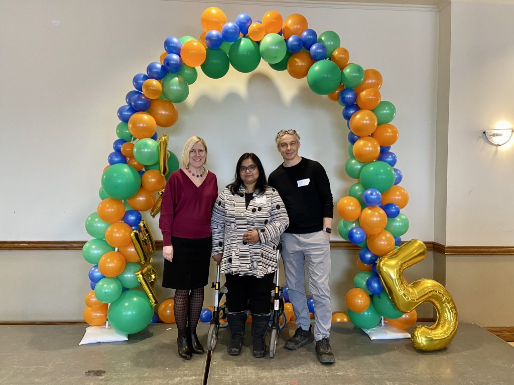 Three people standing under a balloon arch.